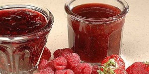 Deux pots de confiture maison devant un tas de fraises et framboises fraiches